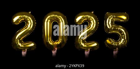 Hands holding glittering golden balloons displaying the numbers 2025, set against a dark background. Perfect for New Year celebrations, festive events Stock Photo