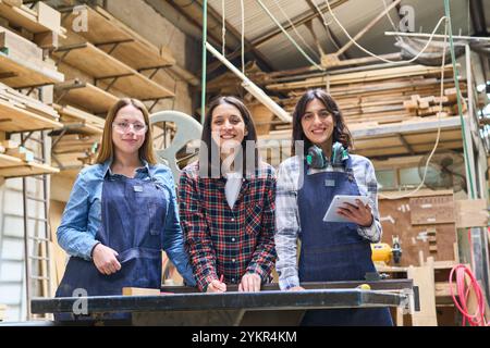 Three female carpenters working together in a bustling lumberyard, showcasing teamwork and craftsmanship. The scene emphasizes training, collaboration Stock Photo