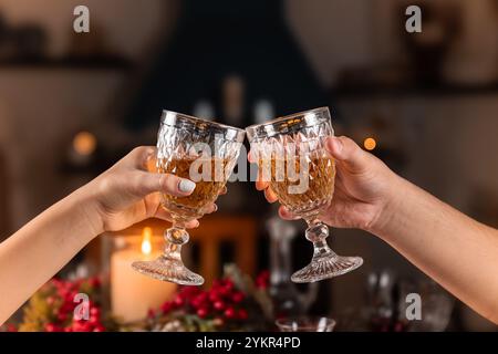 Close-up of two hands raising crystal glasses in a celebratory toast. The warm candlelight and festive decor create a joyful, elegant atmosphere. Stock Photo