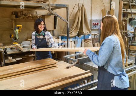 Two women working together in a lumberyard, demonstrating teamwork and collaboration. The environment highlights the industrial setting and the focus Stock Photo