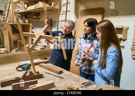 An experienced carpenter guides two younger apprentices in a busy lumberyard workshop. They are collaborating on woodworking projects, fostering teamw Stock Photo