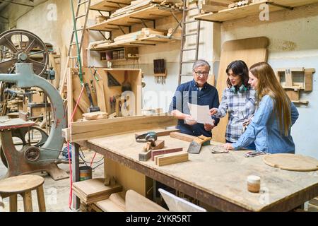 A diverse group of people in a lumberyard collaborating on a woodworking project, emphasizing teamwork, learning, and hands-on skills. The scene captu Stock Photo