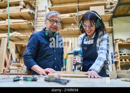 An older and younger worker in a lumberyard collaborate on a woodworking project. The image captures teamwork, skill development, and intergenerationa Stock Photo
