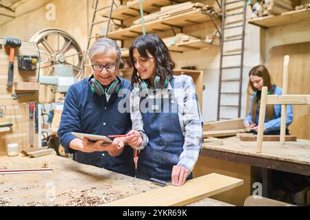 A seasoned craftsman guides a young apprentice in woodworking techniques, highlighting teamwork in a dynamic lumberyard environment. The atmosphere is Stock Photo
