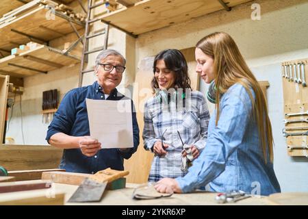 Three lumberyard workers, including an older man and two younger women, engage in teamwork and training. They are discussing plans and collaborating e Stock Photo