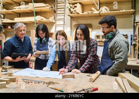 A group of diverse individuals working together in a woodworking shop, emphasizing teamwork, collaboration, and skill development in a lumberyard sett Stock Photo