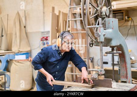 An experienced worker skillfully operates heavy machinery in a busy lumberyard, highlighting precision and craftsmanship in woodworking. The image sho Stock Photo
