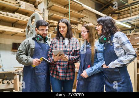 A group of professionals, featuring young apprentices and senior workers, collaborating in a lumberyard. They are engaged in training and teamwork, hi Stock Photo