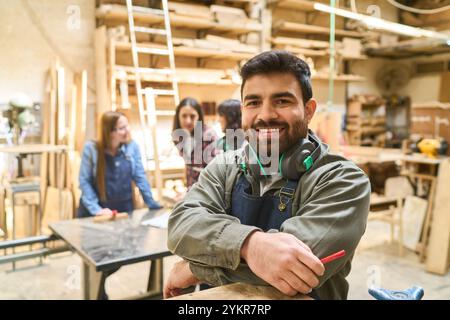A cheerful young worker stands confidently in a bustling lumberyard workshop, surrounded by colleagues engaged in teamwork and learning. The scene hig Stock Photo
