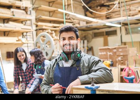 Smiling young professionals working together in a bustling lumberyard. Emphasizing teamwork, craftsmanship, and apprenticeship in a woodshop environme Stock Photo