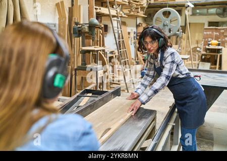 A lively lumberyard scene showing younger and older workers collaborating and engaging in teamwork. Both are focused and wearing protective gear while Stock Photo