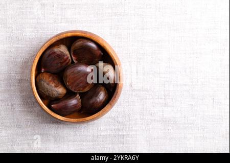 Sweet chestnuts in a wooden bowl on linen, from above, with empty space for text. Castanea sativa, raw, whole and unshelled. Stock Photo