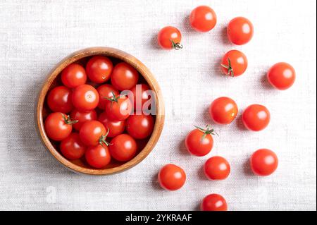 Small red cherry tomatoes in a wooden bowl on linen fabric, from above. Fresh, ripe, tiny and round cocktail tomatoes. Stock Photo