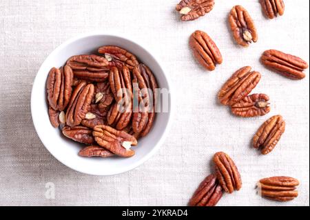 Pecan halves in a white bowl on linen fabric. Shelled and dried pecan nuts, seeds and fruits of Carya illinoinensis. Stock Photo