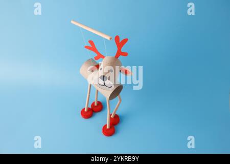 DIY reindeer puppet made from cardboard tubes, red bottle caps, and paper details. Blue background. Christmas craft and holiday decoration concept. to Stock Photo