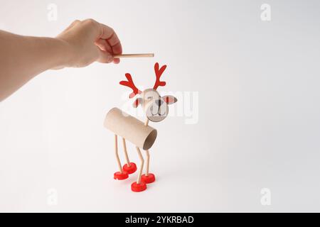 Hand holding DIY reindeer puppet made from cardboard tubes, plastic caps, and paper details. Christmas craft and holiday decoration concept, easy acti Stock Photo