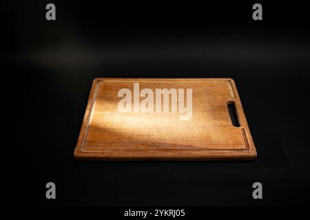 Minimal culinary backdrop with a rectangular wooden chopping board and a light ray, on black Stock Photo