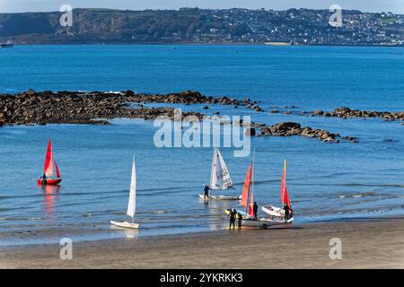 Yachts with red and white sails launching off the beach at Marazion on a sunny autumnal morning, Cornwall England UK Stock Photo