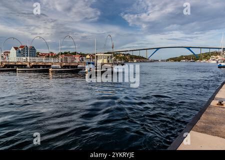 The Queen Emma Bridge (Koningin Emmabrug) at Sint Annabaai in Willemstad, Curaçao, fully open – a view from the Punda waterfront of the clear passage for ships. In the background is the Queen Juliana Bridge, which has carried road traffic since 1974. The Queen Emma Bridge is called the Swinging Old Lady. This 1888 pontoon pedestrian bridge opens laterally for passing ships. Handelskade, Willemstad, Curaçao, Kòrsou Stock Photo