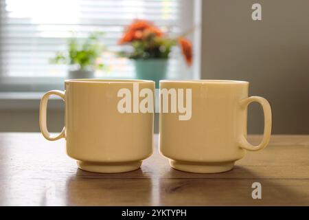 White ceramic coffee cups on kitchen table, cozy home interior, flowers on window Stock Photo