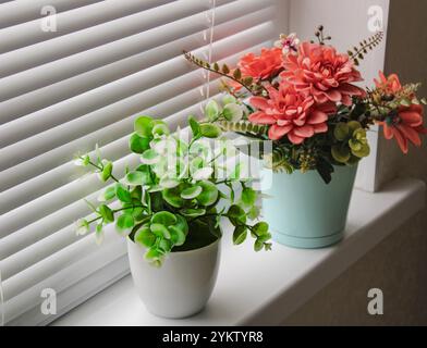 Bright artificial plants in pots on the windowsill, red flowers on the window Stock Photo