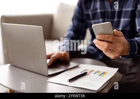 Unrecognizable Business Guy Using Phone And Laptop Indoors, Cropped Stock Photo