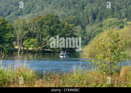 Small boat at the southern tip of Lake Windermere as it turns into the river Leven near Newby Bridge. Lake District, England. Stock Photo