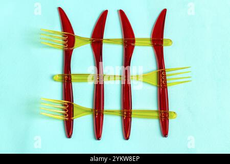 Red plastic disposable knives and yellow forks. Isolated on turquoise background Stock Photo