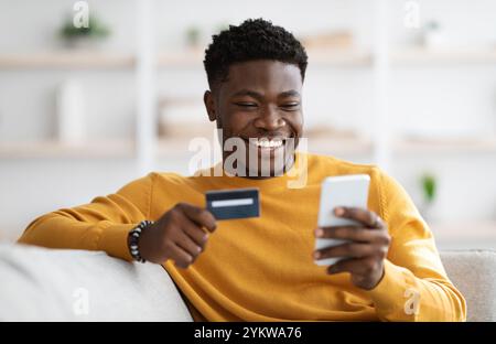 Positive black man using cellphone and credit card at home Stock Photo