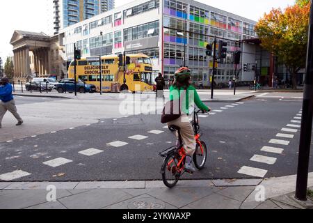 Young woman student cyclist crossing road riding bike outdide UAL College of Communication Elephant & Castle building in South London UK  KATHY DEWITT Stock Photo