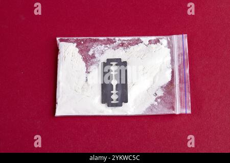 Razor and pack of cocaine powder for snorting isolated on red. Top view close-up Stock Photo