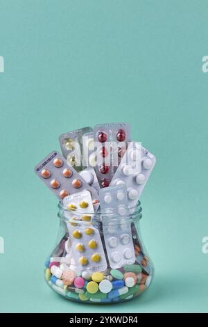 Medical pills and blisters in glass jar on turquoise background. Space for text Stock Photo