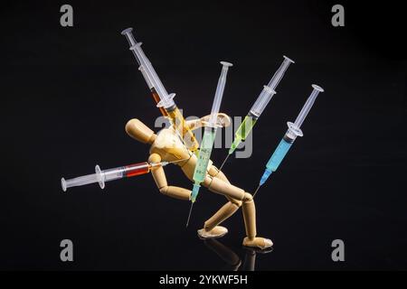 Composition of wooden mannequin with stucked syringes on black background. Drug addiction concept Stock Photo