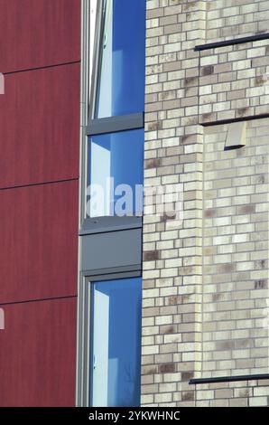 Modern building facade showcasing a blend of brick, red paneling, and blue window reflections, highlighting contemporary architectural design Stock Photo