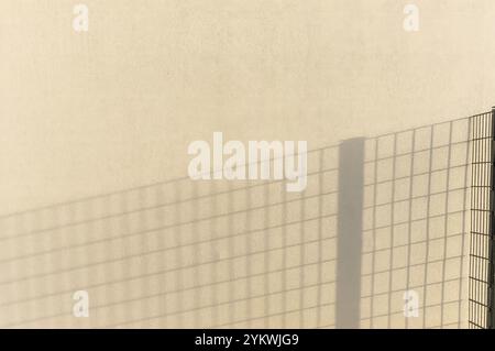 Shadow of a fence is being cast on a beige wall, creating a geometric pattern Stock Photo