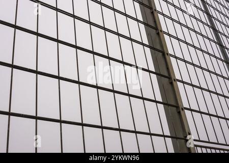 Close-up of a metal mesh wire fence, forming a regular grid pattern against a soft, overcast sky Stock Photo