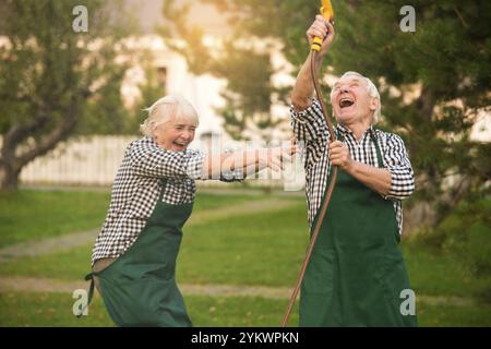 Couple having fun, water hose. Cheerful senior people outdoors. You are never too old Stock Photo