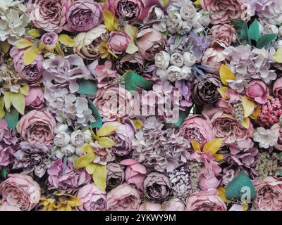 beautiful textured background of many artificial fabric flowers, fake peonies, roses and various blooming flowers in the decor of rooms and surfaces Stock Photo