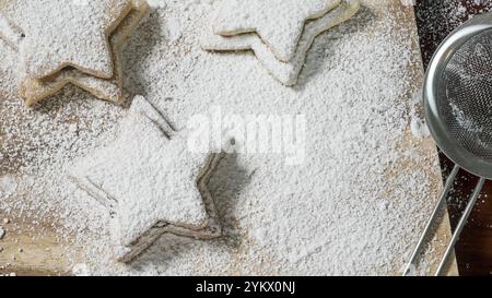 Several star-shaped cookies lie on a surface, freshly coated with powdered sugar using a sifter. The scene suggests a recent baking session. Stock Photo