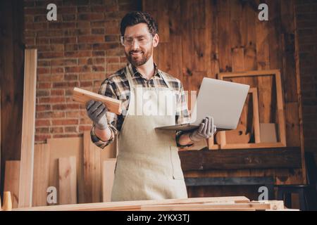 Photo of workman guy hold laptop look plank timber in workshop garage Stock Photo