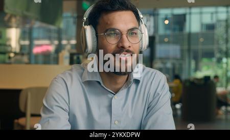 Indian ethnic guy male businessman freelancer visitor cafe drink coffee break smiling business man listen music headphones drinking tea in restaurant Stock Photo