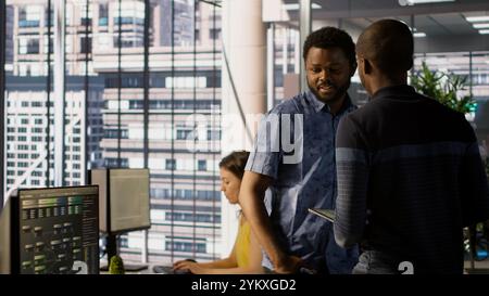 Managers evaluating work done by computer scientists in workspace doing software debugging. Management executives walking in office with tablet, checking code fixed by employees, camera A Stock Photo