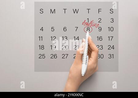 Woman marking date of deadline in calendar on grey background Stock Photo