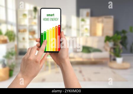 Hands holding mobile phone with energy efficiency rating on screen in room Stock Photo