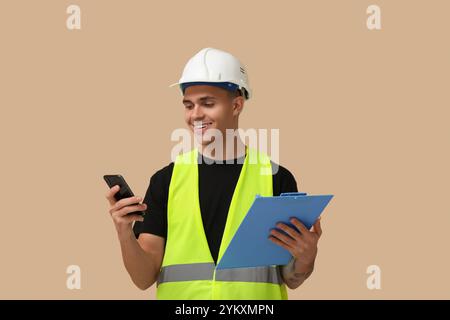 Young male engineer with clipboard and mobile phone on beige background Stock Photo