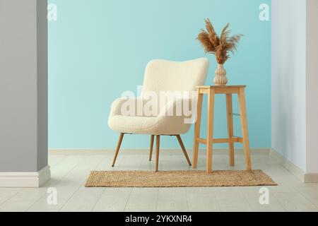 White armchair and pampas grass in vase near blue wall Stock Photo