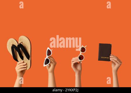 Female hands with stylish sunglasses, flip flops and passport on orange background Stock Photo