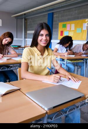 Portrait happy young Caucasian woman student sitting at desk with classmates in classroom.  Stock Photo
