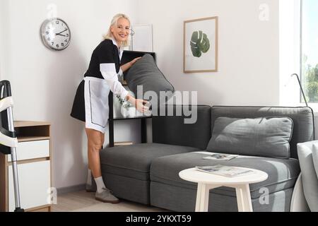 Middle-aged chambermaid adjusting pillows on sofa in hotel room Stock Photo