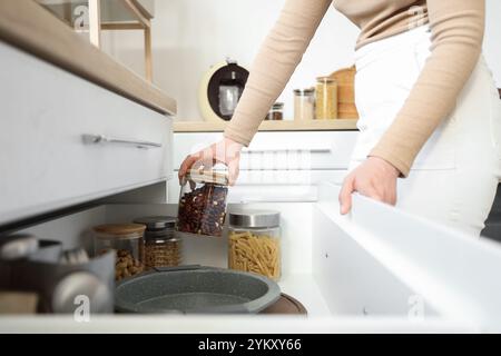 Woman taking jar of nuts from open drawer in kitchen, closeup Stock Photo